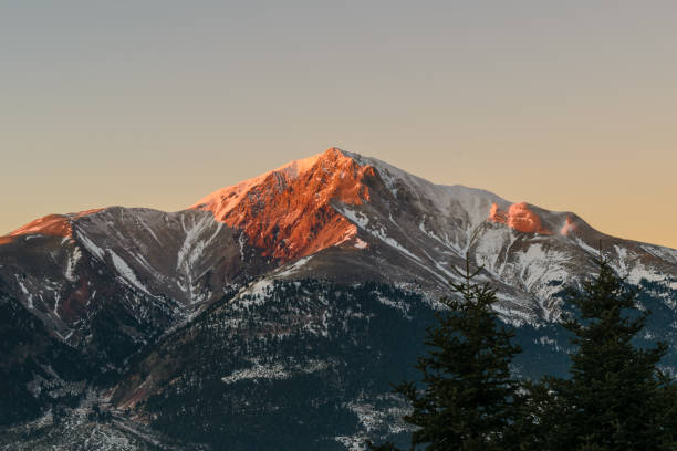 istock Mountain peak at sunset with fir trees in foreground and snow 1049923016