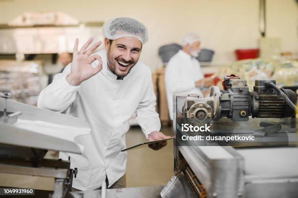 Foto de Boa Qualidade Retrato De Uma Jovem Sorridente Alegre Roupa Estéril Em Fábrica De Alimentos Segurar O Tablet Com Uma Mão E Com Outros Gesticulando Que A Qualidade Do Produto É Bom e mais fotos de stock de Comida