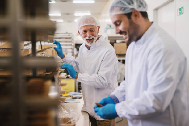 bild von zwei männlichen essen fabrikarbeiter in sterile kleidung verpacken frische plätzchen und spaß haben. - hair net stock-fotos und bilder