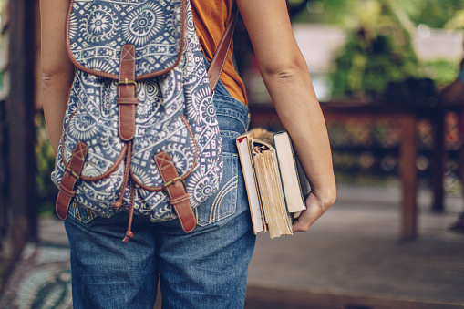One woman, university student girl holding book, and wearing a backpack., rear view.