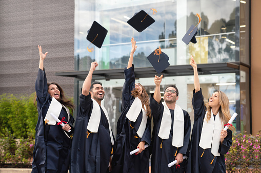 Happy group of students celebrating their graduation throwing their mortar boards in the air - education concepts