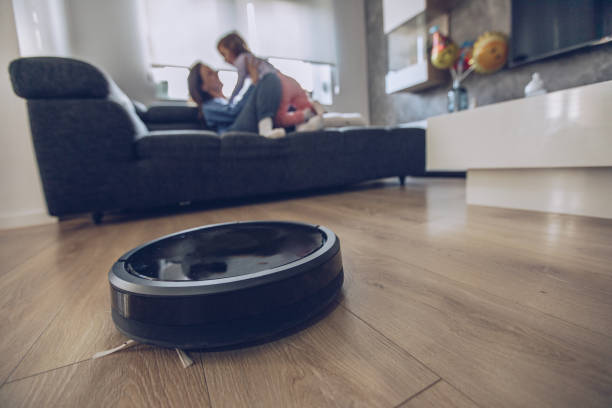 Time to relax at home One woman, at home relaxing with her little daughter on sofa, while robot vacuum cleaner is working. smart home family stock pictures, royalty-free photos & images