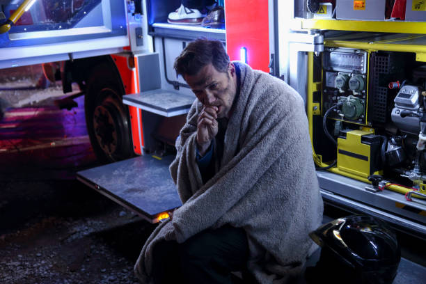 Big fire victim sitting on a firefighter's truck Man with blanket sitting at firemen truck. Black from smoke and fire. Burn Injuries stock pictures, royalty-free photos & images