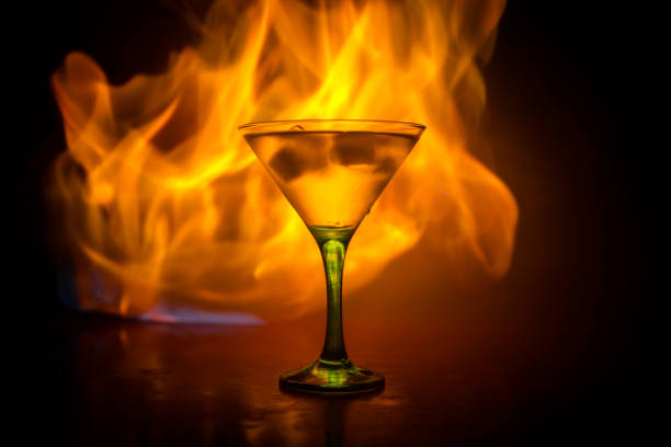 martini in feuer-konzept. glas des berühmten cocktail martini brennen bei feuer im dunkel getönten nebligen hintergrund. - martini brand vermouth stock-fotos und bilder