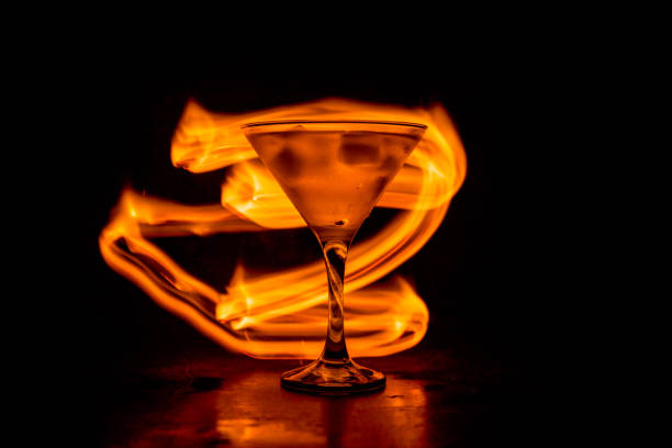 martini in feuer-konzept. glas des berühmten cocktail martini brennen bei feuer im dunkel getönten nebligen hintergrund. - martini brand vermouth stock-fotos und bilder