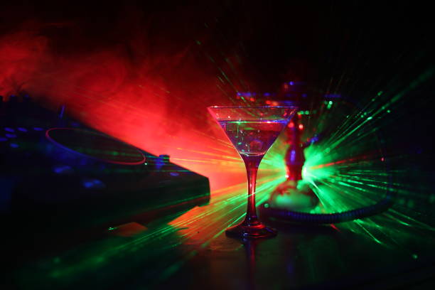 istock Glass with martini with olive inside on dj controller in night club. Dj Console with club drink at music party in nightclub with disco lights. 1049991532