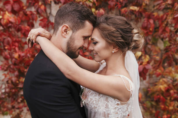 화려한 신부 그리고 세련 된 신랑 부드럽게 포옹 하 고 벽의 붉은 단풍에 웃 고. 행복 한 감각적인 웨딩 커플 수용입니다. 신혼의 로맨틱 한 순간 - couple autumn fashion male beauty 뉴스 사진 이미지