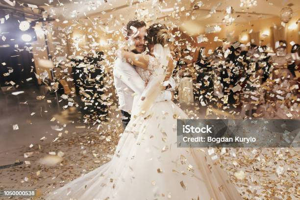 Gorgeous Bride And Stylish Groom Dancing Under Golden Confetti At Wedding Reception Happy Wedding Couple Performing First Dance In Restaurant Romantic Moments Stock Photo - Download Image Now