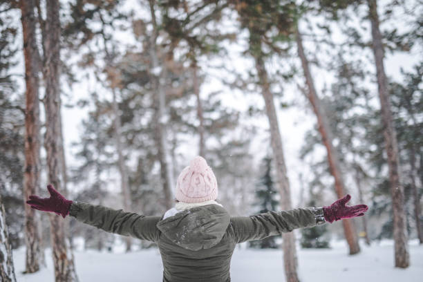 Young woman in a snowy forest, spreading hands in joy