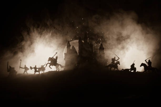 Medieval battle scene with cavalry and infantry. Silhouettes of figures as separate objects, fight between warriors on dark toned foggy background with medieval castle. Selective focus