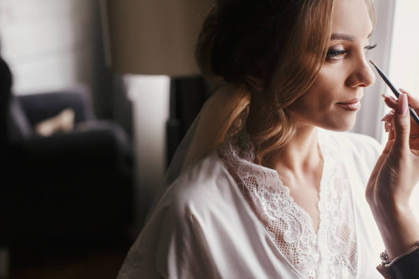 novia con estilo para su maquillaje por la mañana a la luz de la ventana. artista de maquillaje haciendo las cejas y aplicar sombra de ojos en primer plano de cara de la novia. - bride veil women human face fotografías e imágenes de stock