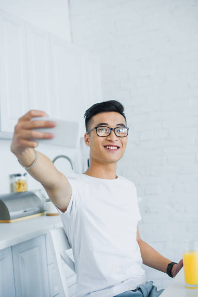 istock smiling young asian man in eyeglasses taking selfie with smartphone in kitchen 1050012540
