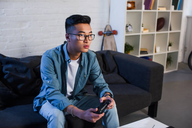 istock focused young asian man playing video game with joystick at home 1050012596