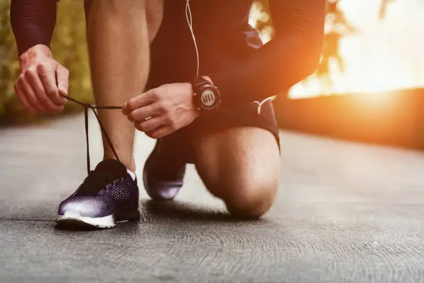 Photo of Close-up of sportsman tying sneakers. Unrecognizable man stopping lacing shoe outdoors. Athletic shoes concept.