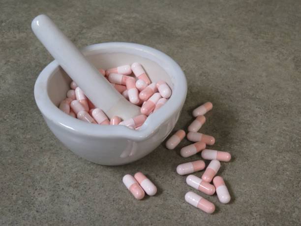 Capsules in mortar Pink and white gelatin capsules in a white, ceramic (wedgewood) mortar with pestle on a compounding pharmacy countertop. pharmaceutical compounding stock pictures, royalty-free photos & images