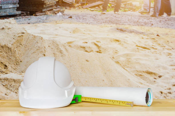 casco bianco plastica con progetto piano rotolo di carta e nastro di misura verde su tavolo in legno in cantiere edificio abitativo con spazio di copia aggiungere testo - house construction tape measure blueprint foto e immagini stock