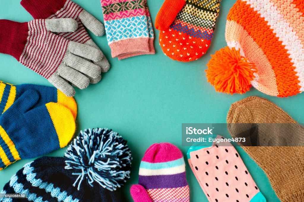 Caps, mittens, gloves and socks are stacked in a circle. View from above. Warm clothes in the form of hats, mittens, gloves and socks for autumn and winter. Warm clothes for cold seasons. Warm Clothing Stock Photo