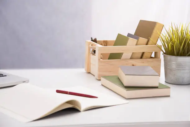 The wooden box with book put beside tree pot and book stacked,on desk,blurry light around