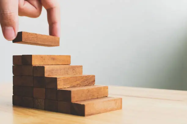 Photo of Hand arranging wood block stacking as step stair. Ladder career path concept for business growth success process