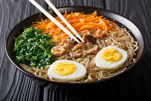 Asian food: soba soup with vegetables, shiitake mushrooms, egg and sesame seeds close up in a bowl. horizontal