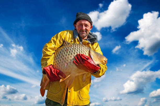 istock Fisherman Holding a Big Fish Against Blue Sky and Clouds 1050151838