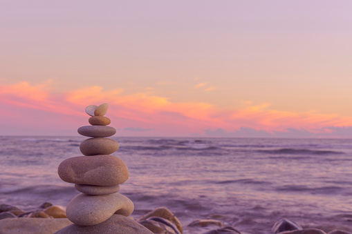 Pyramid of stones of light color against the background of the sea and the sunset sky. Balance of round pebbles against the backdrop of a beautiful sunset.