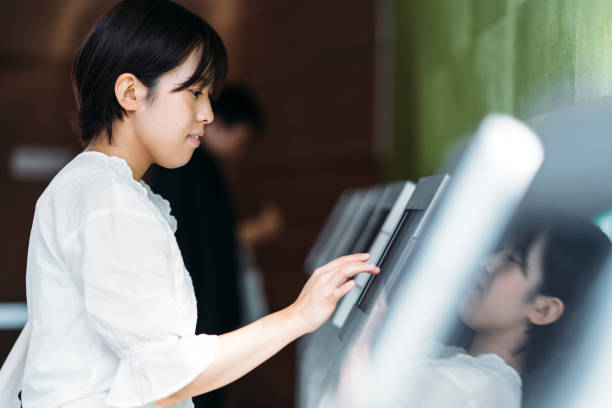 Young woman using digital device at counter A young woman is using a digital electronic check in device at a counter. airport check in counter stock pictures, royalty-free photos & images