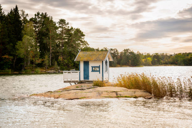 Photo of Beautiful landscape view of a small bath hut cottage on a rock in a lake surrounded by trees and reed.