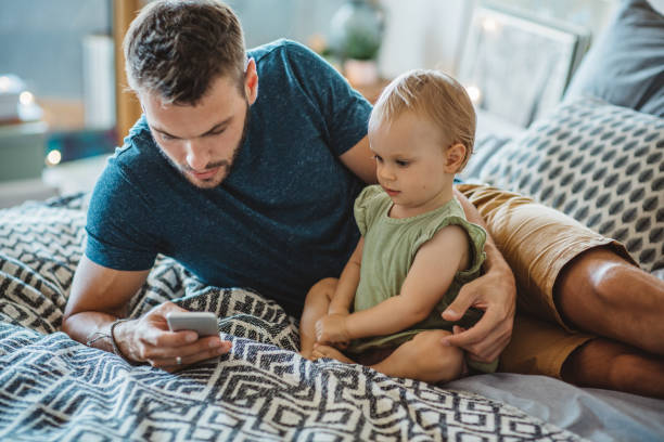 padre muestra a pequeña hija algo en el teléfono - working bed smart phone bedroom fotografías e imágenes de stock