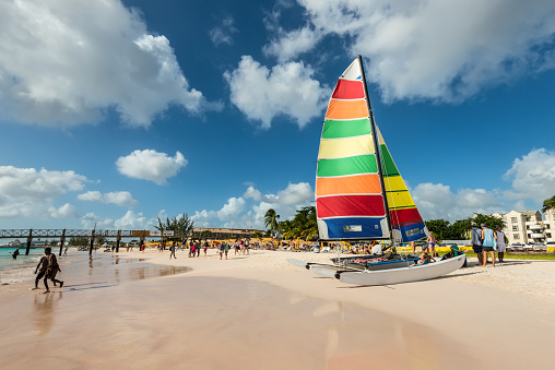 Bridgetown, Barbados - December 18, 2016: Brownes beach at ocean coast with people and colorful sail on a yacht at sunny day in Bridgetown, Barbados.