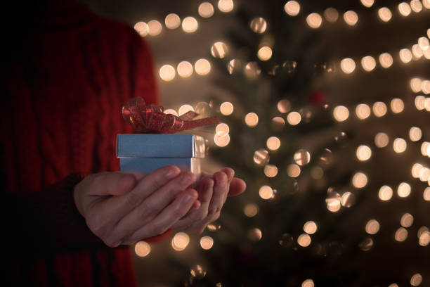 istock Holding gift box with red bow against blurred Christmas lights 1050196832