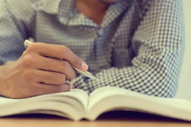 Photo of close up student man hand holding pen for guideline reading on text book at campus library for examination education concept