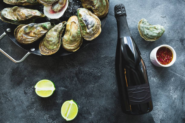 Raw oysters with bottle of alcohol drink and limes on dark table. Flat lay. Top view. Food background