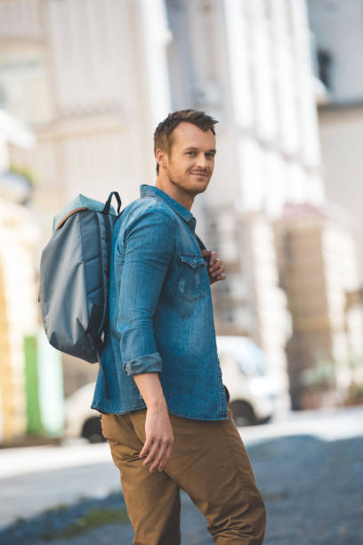 istock attractive young tourist with backpack walking by street and looking at camera 1050239038