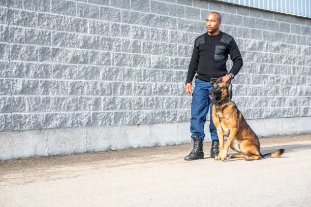 A portrait of a real, trained, K-9 dog handler outside of an industrial building.