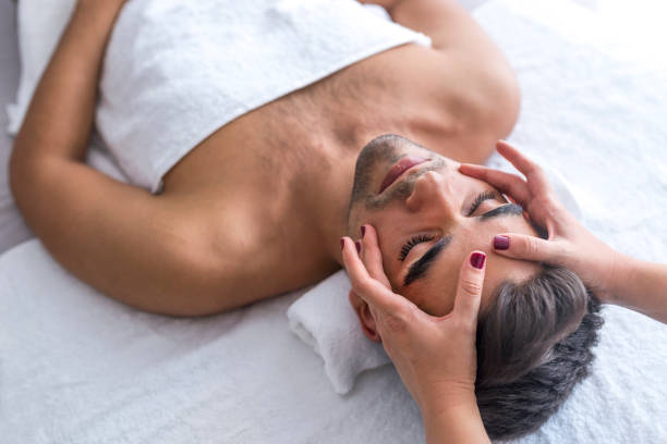 bellezza maschile - uomo che riceve un massaggio facciale presso un centro benessere di lusso - massaging spa treatment health spa men foto e immagini stock