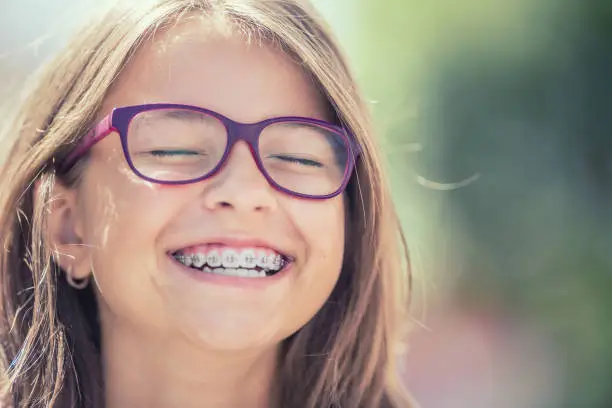 Portrait of a happy smiling teenage girl with dental braces and glasses.