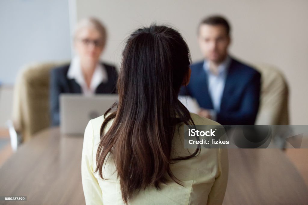 Businesswoman and businessman HR manager interviewing woman Businesswoman and businessman HR manager interviewing woman. Candidate female sitting her back to camera, focus on her, close up rear view, interviewers on background. Human resources, hiring concept Job Interview Stock Photo