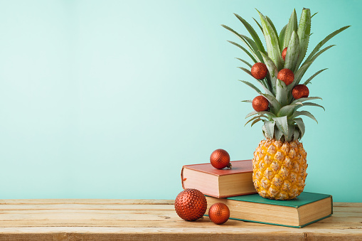 Christmas holiday concept with  pineapple as alternative Christmas tree and books on wooden table over mint background