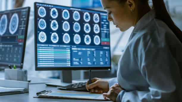istock Female Medical Research Scientist Working with Brain Scans on Her Personal Computer, Writing Down Data in a Clipboard. Modern Laboratory Working on Neurophysiology, Science, Neuropharmacology. 1050311504