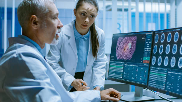 istock Two Medical Scientists in the Brain Research Laboratory Discussing Progress on the Neurophysiology Project Curing Tumors. Neuroscientists Use Personal Computer with MRI, CT Scans Show Brain Images. 1050311526