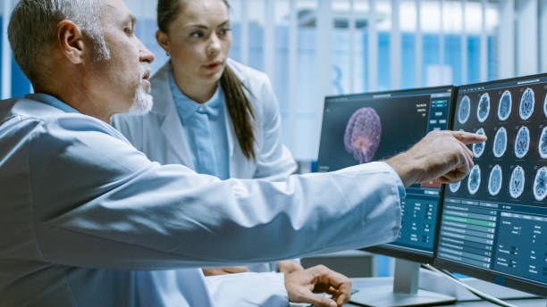 istock Two Medical Scientists in the Brain Research Laboratory Discussing Progress on the Neurophysiology Project Curing Tumors. Neuroscientists Use Personal Computer with MRI, CT Scans Show Brain Images. 1050311530