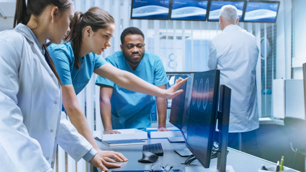 istock Diverse Team of Medical Scientists Solve Problems and Point at Computer Screens Showing CT, MRI Scans. Neurologists / Neuroscientists Working in Brain Research Laboratory. 1050311816