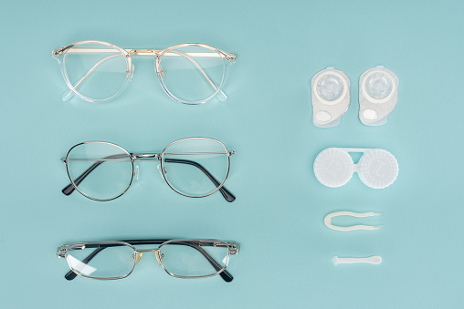 top view of eyeglasses, contact lenses containers and tweezers arranged on blue background