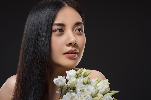 portrait of asian woman with beautiful dark hair and bouquet of white eustoma flowers isolated on black