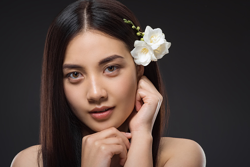 portrait of beautiful young asian woman with white flowers in hair looking at camera isolated on black