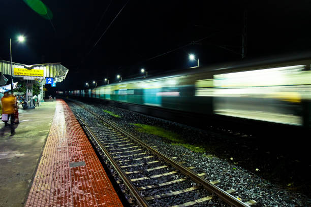 Bishnupriya Halt, WB, India - August 25, 2018 : Taken this picture in state of West Bengal India of a railway station. It was a full moon night and the platform is dark. ON the platform under the shade passengers are waiting for their respective trains to arrive. The high speed train passing by and blurr motion. People walking on the platform waiting for their train. The high speed intercity train crossing the railway station.