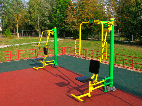 Modern sports equipments for muscle training. Sports ground outdoor with artificial covering. In the background are trees.