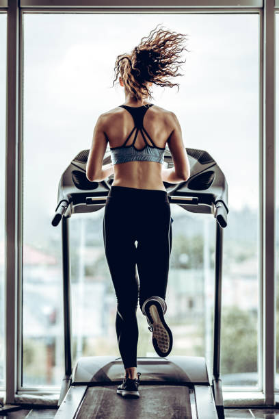 Beautiful attractive woman runs on the running track Beautiful attractive woman with curly long hair runs on the running track, fitness on the treadmill, woman maintains an excellent shape in the gym, fit body, perfect body shape treadmill photos stock pictures, royalty-free photos & images