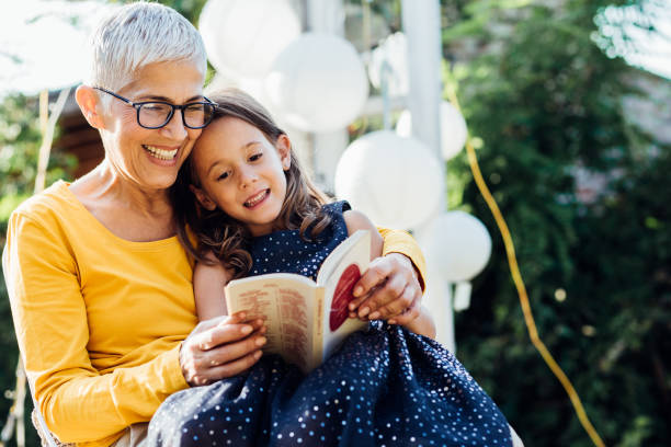 smiling woman reading to granddaughter - woman with glasses reading a book imagens e fotografias de stock